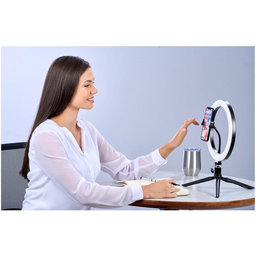 A ring light shown in use by a woman sitting at a desk.
